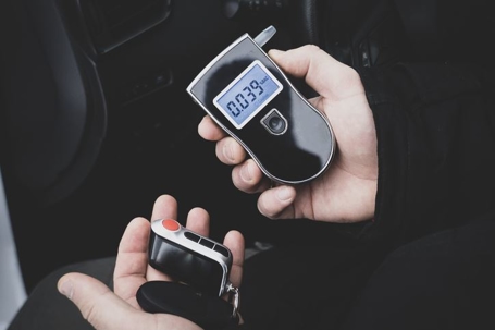 Image of hands holding a set of keys and a breathalyzer