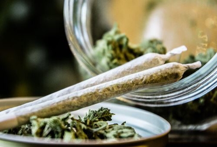 Marijuana joints on plate in front of jar full of cannabis